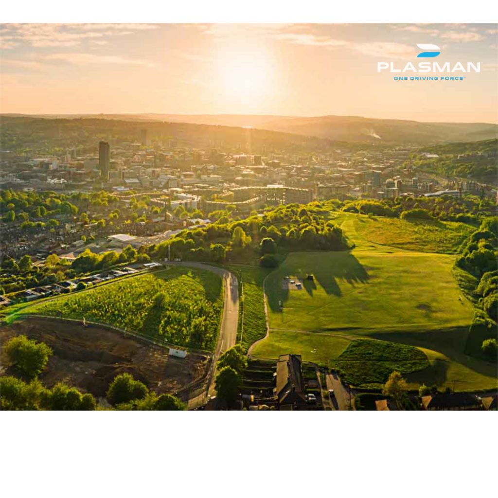 Sun rising over skyline of green forested area surrounding a city with Plasman logo in top right corner