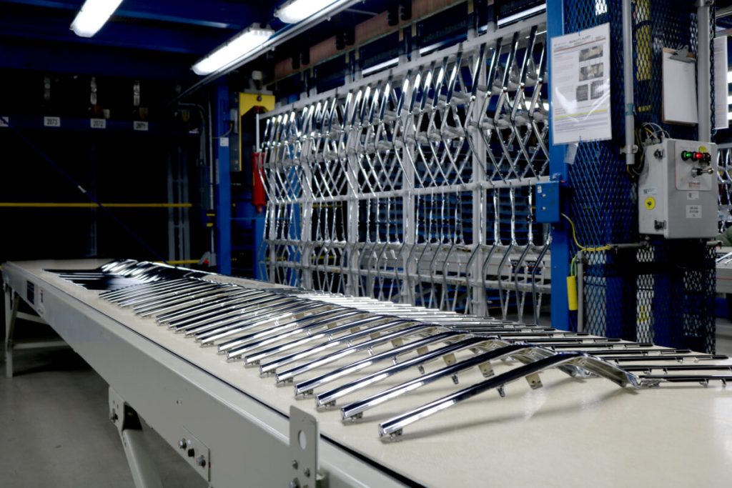 Chromed car parts lined up on conveyer belt in front of rack full of the same chromed parts at Plasman Cleveland Manufacturing