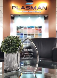 Plasman Outstanding Employee Engagement 2021 glass award on table in front of leather chair and wall with Plasman logo at Global Headquarters