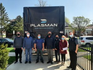 Employees from Plasman and Windsor Residence for Young Men wearing masks and standing outside in front of large Plasman truck after giving donation