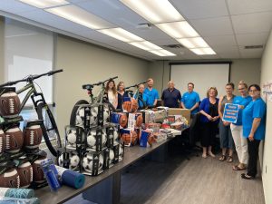 Group of Plasman MVPs and Maryvale employees posing around table full of sports equipment, toys, books, and more for donation to Maryvale