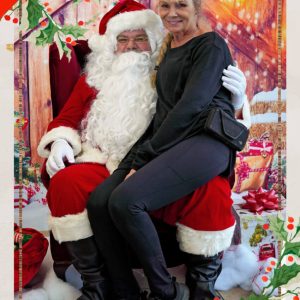 Plasman employee sitting on Santa's lap in front of presents and barn wood wall