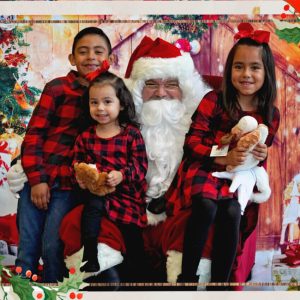 Three children sitting on Santa's lap on a a red chair in front of a Christmas tree 