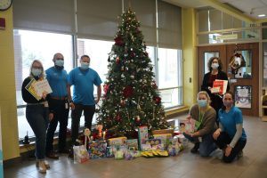 Group of Plasman and John McGivney Children's centre employees standing around Christmas tree with toys and book donation underneath 