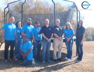 Group of Plasman Fort Payne Manufacturing employees in cyan t-shirts stand in front of trampoline donated to Southeastern Children's Home