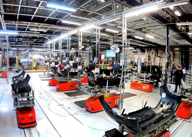 Red robots holding black front bumpers with employees assembling parts in factory