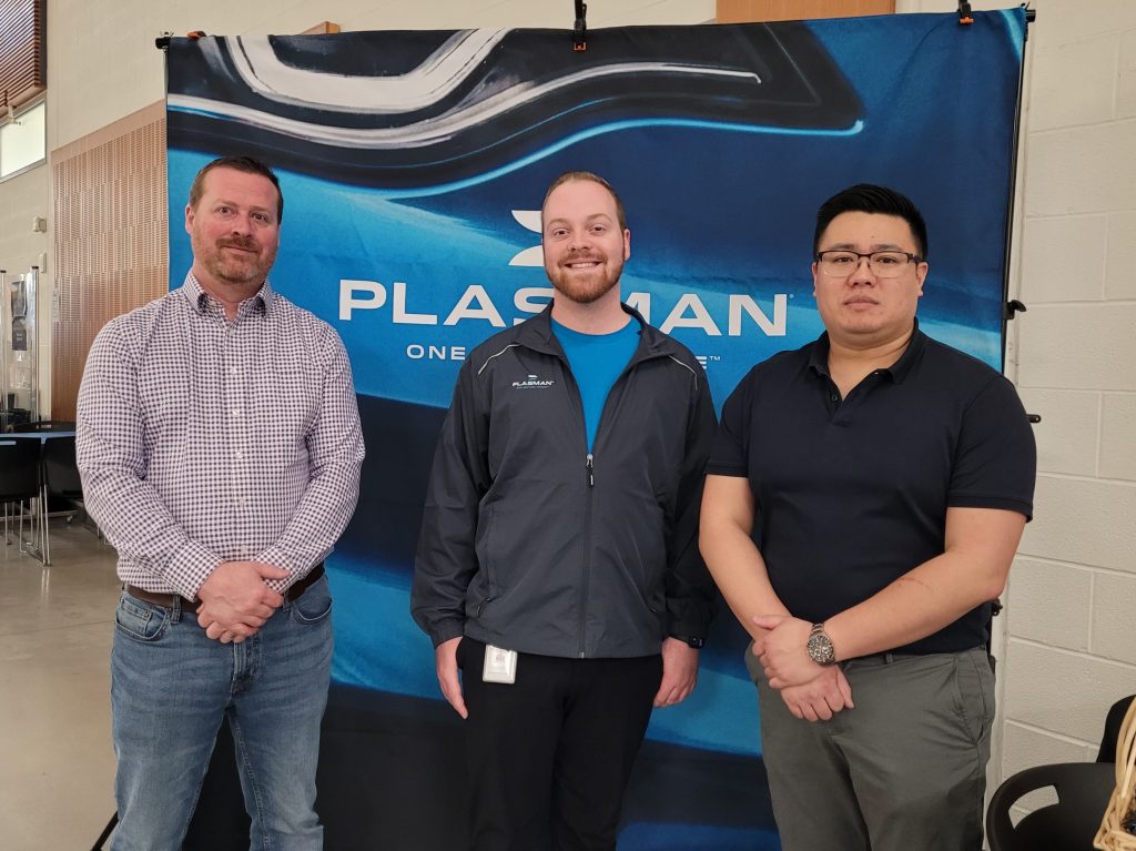 Photo of 3 Plasman employees in front of a Plasman branded backdrop