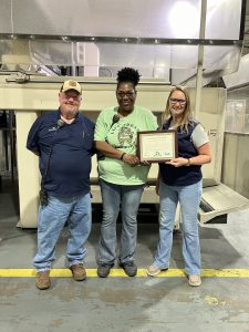 Three Plasman employees on plant floor holding the award certificate