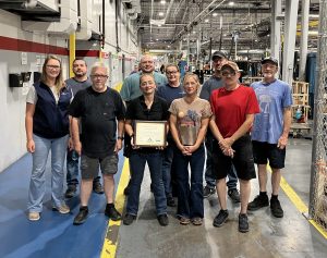 Group of Plasman employees on plant floor middle person holding certificate award