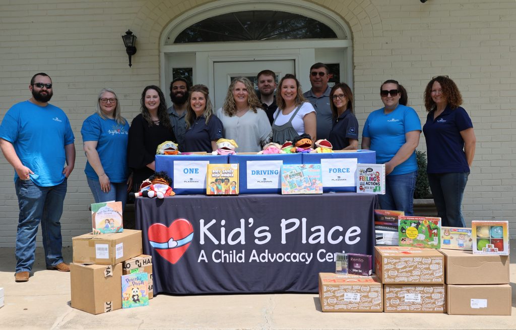 A group of MVP ambassadors from Plasman and Kid's Place representatives standing behind boxes of donations on the front porch of the Kid's Place center