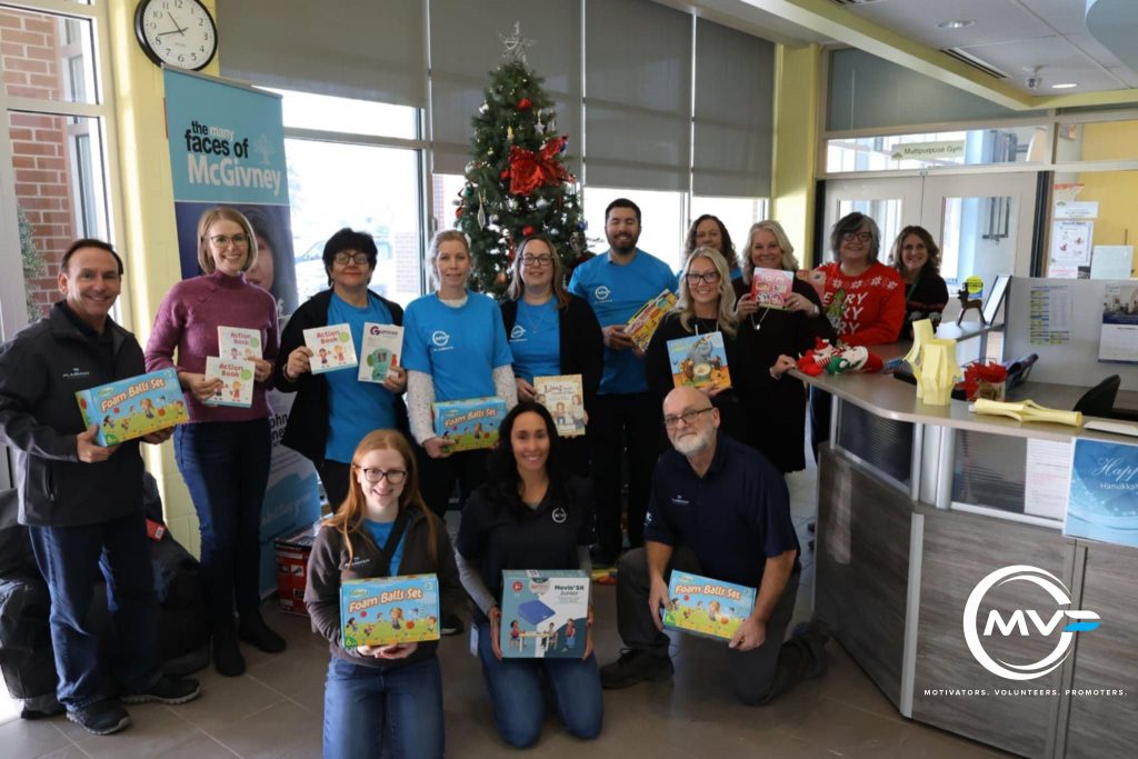 Group of both JMCC representatives and Plasman MVPs in front of a Christmas tree holding donated items