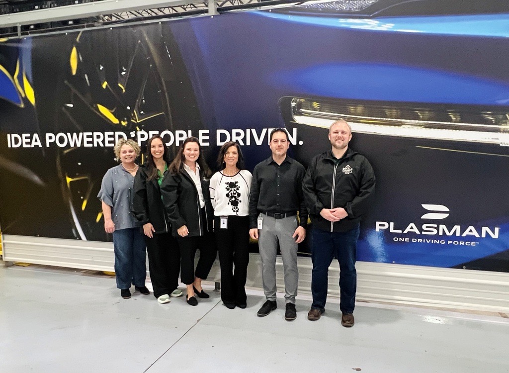 DCEDA and Plasman members standing in front of a wall with a car on it and Plasman's logo