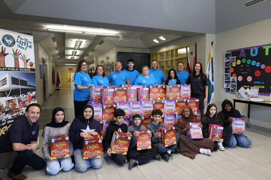 Group of Plasman MVP ambassadors standing behind four rows of cereal boxes and children sitting in front holding cereal boxes